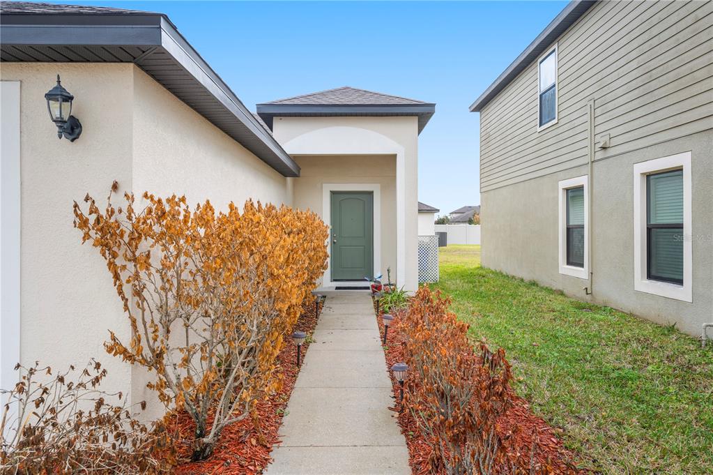 A concrete walkway leads to a green front door between two residential buildings — 6551 BAIKAL PLACE, LAKELAND, FL