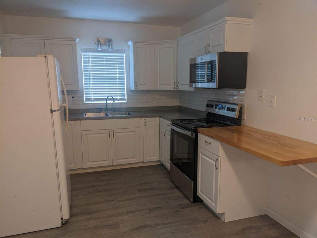 A kitchen features white cabinets, stainless steel appliances, a gray countertop, and wood-topped breakfast bar — 729 VIRGINIA AVENUE, AUBURNDALE, FL