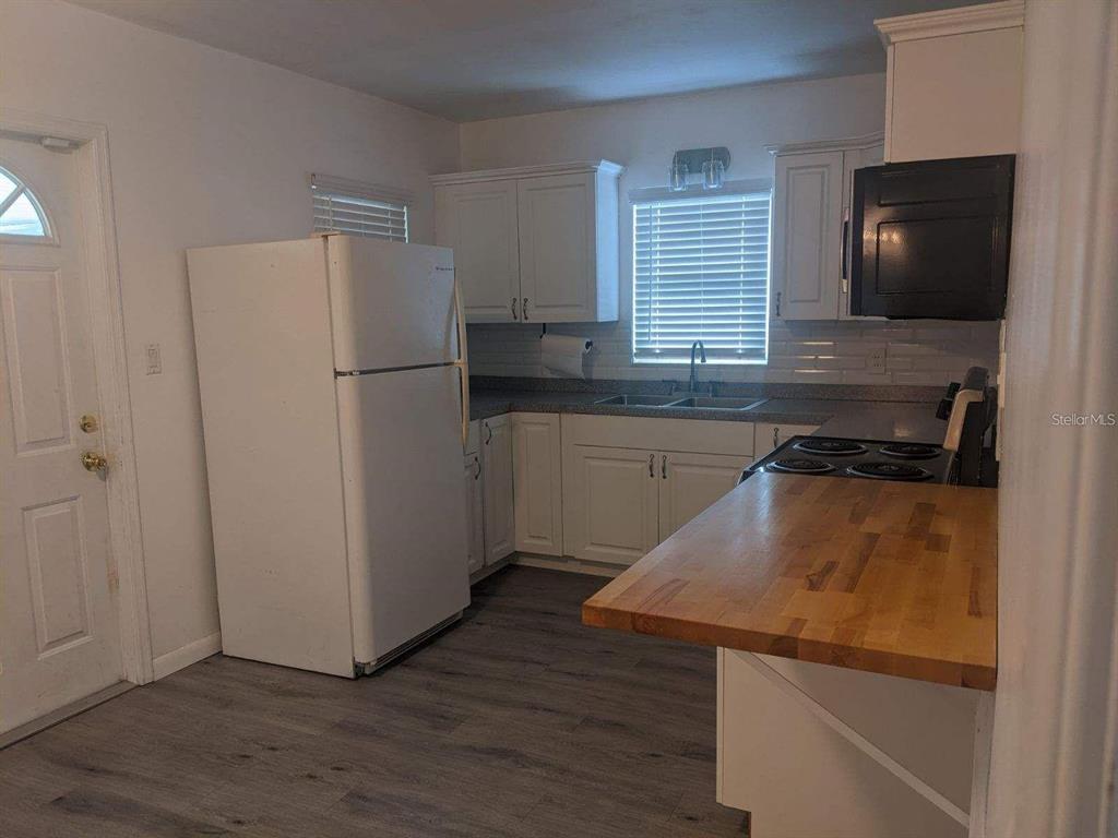 A kitchen features white cabinets, a white refrigerator, a butcher block countertop, and gray flooring — 729 VIRGINIA AVENUE, AUBURNDALE, FL