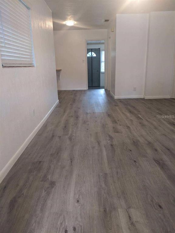 A room with light gray wood-look flooring and white walls leads to an exterior door — 729 VIRGINIA AVENUE, AUBURNDALE, FL