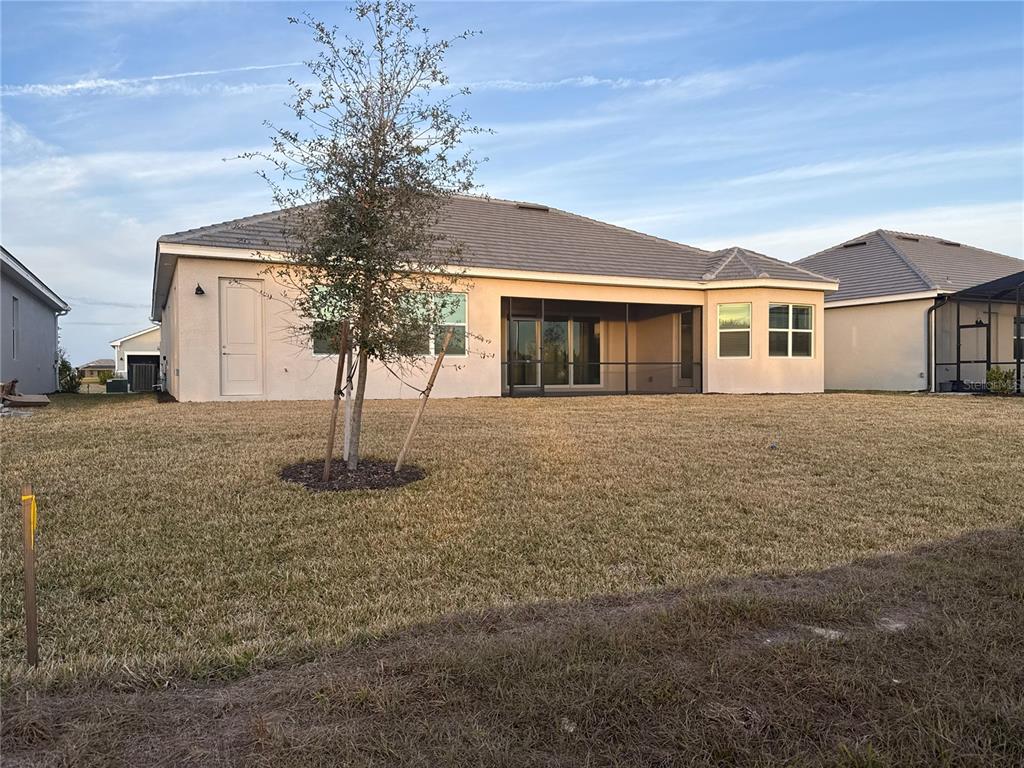 The rear exterior of a single-story house with a screened-in lanai and a grassy yard — 7796 LAKES EDGE LANE, PORT CHARLOTTE, FL