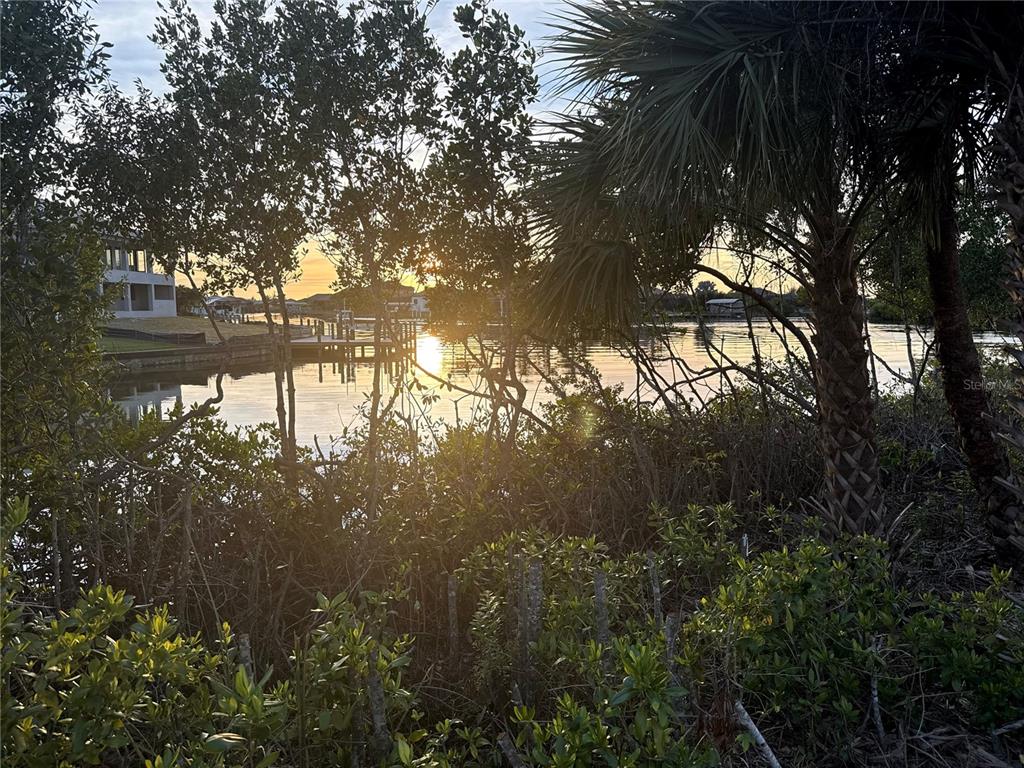 A view of a sunset over a canal with a wooden dock and surrounding trees — 7796 LAKES EDGE LANE, PORT CHARLOTTE, FL