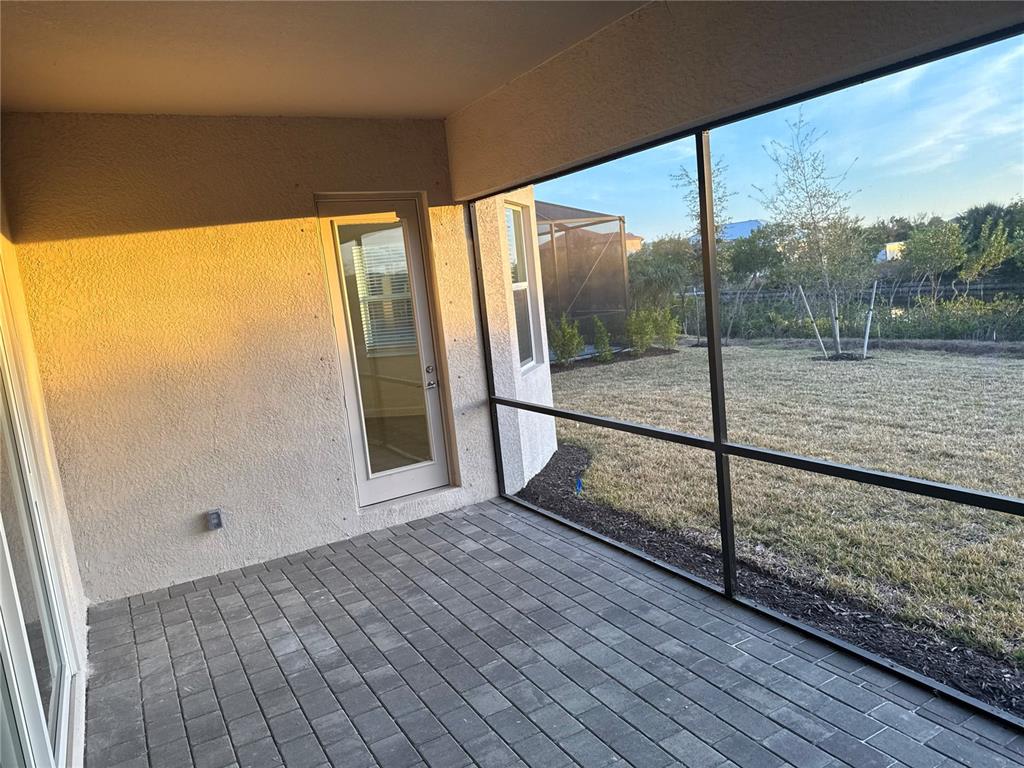 A covered patio with gray paver flooring and a screened-in view of a grassy yard — 7796 LAKES EDGE LANE, PORT CHARLOTTE, FL