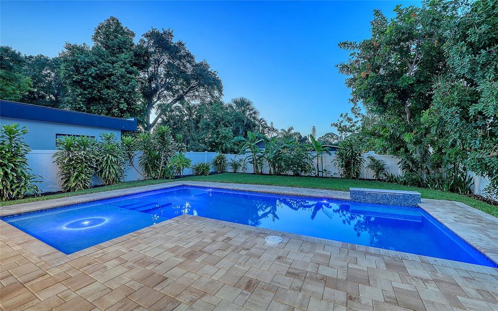 A rectangular swimming pool with a tanning ledge sits on a paved patio near trees — 2483 BAY STREET, SARASOTA, FL