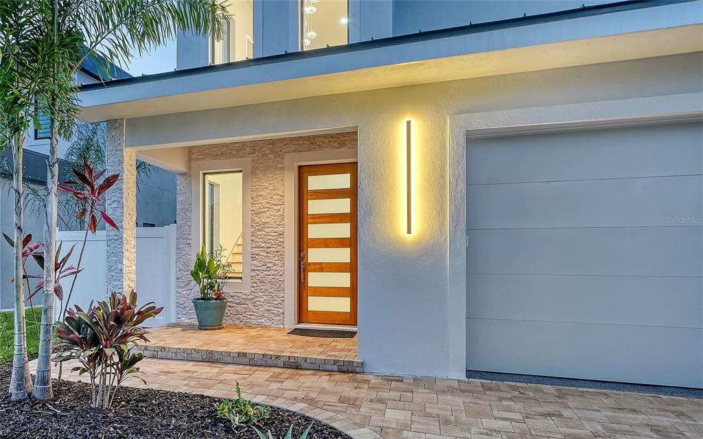 The exterior of a modern home features a stone-accented entryway, a wooden door, and garage — 2483 BAY STREET, SARASOTA, FL
