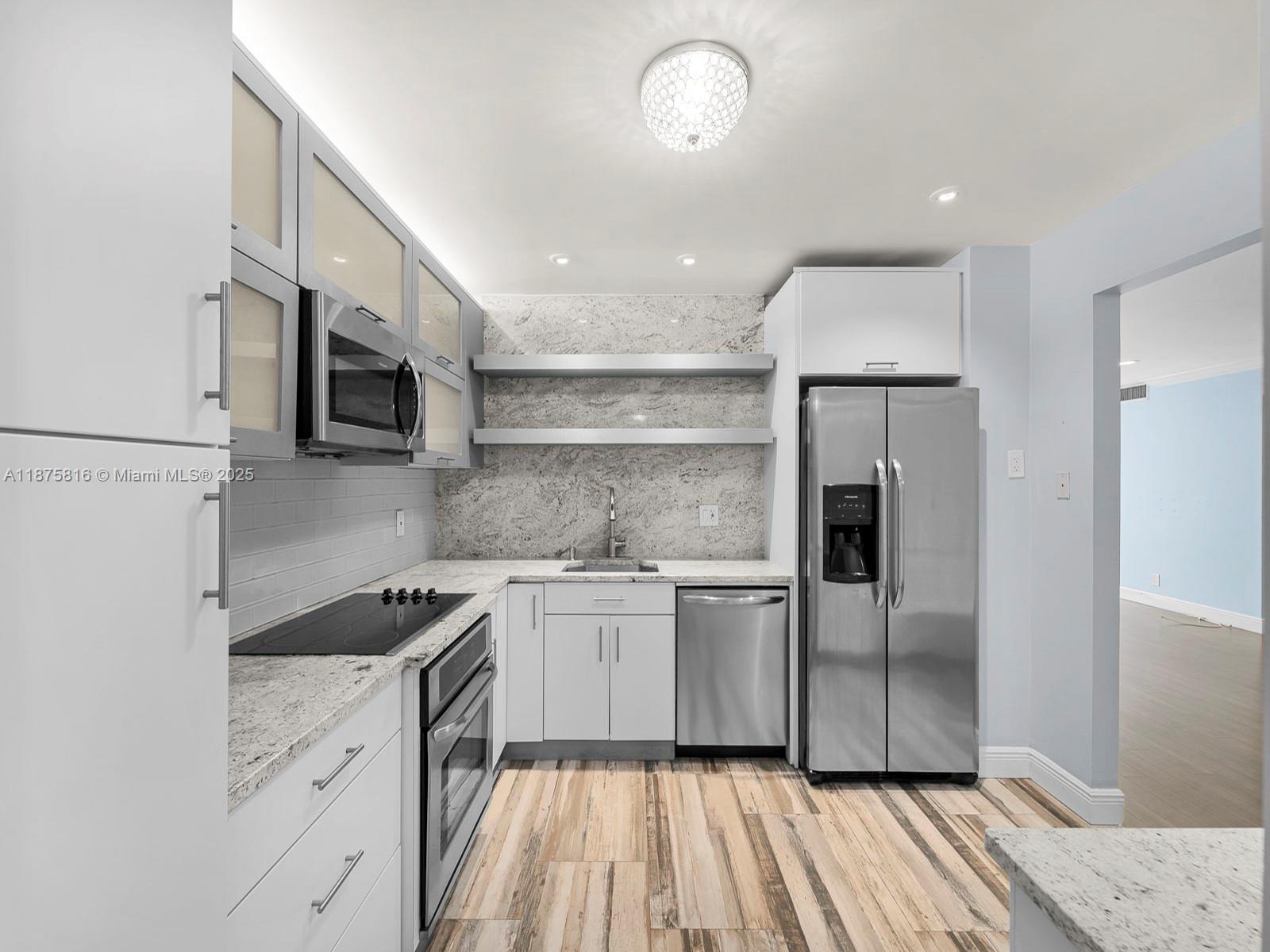 A modern kitchen features white cabinets, stainless steel appliances, granite countertops, and wood-look tile flooring — 2301 S Ocean Dr # 307, Hollywood FL 33019, HOLLYWOOD, FL