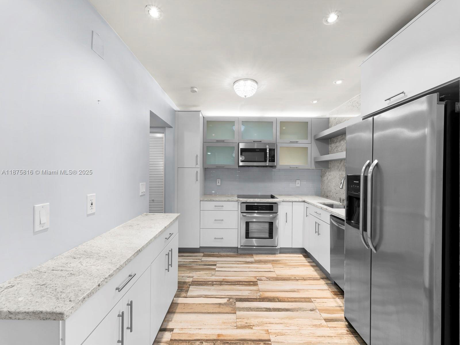 A kitchen features white cabinetry, stainless steel appliances, granite countertops, and wood-look tile flooring — 2301 S Ocean Dr # 307, Hollywood FL 33019, HOLLYWOOD, FL
