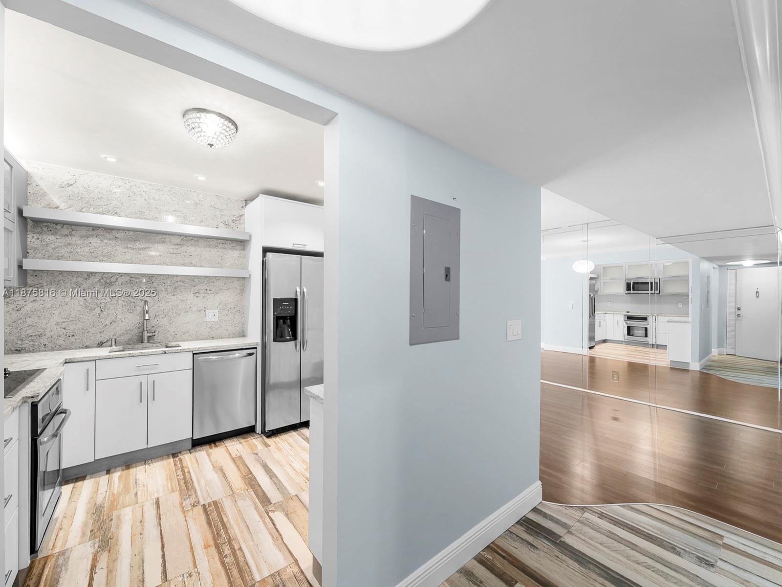 A kitchen with white cabinets, stainless steel appliances, and stone countertops opens to a hallway — 2301 S Ocean Dr # 307, Hollywood FL 33019, HOLLYWOOD, FL
