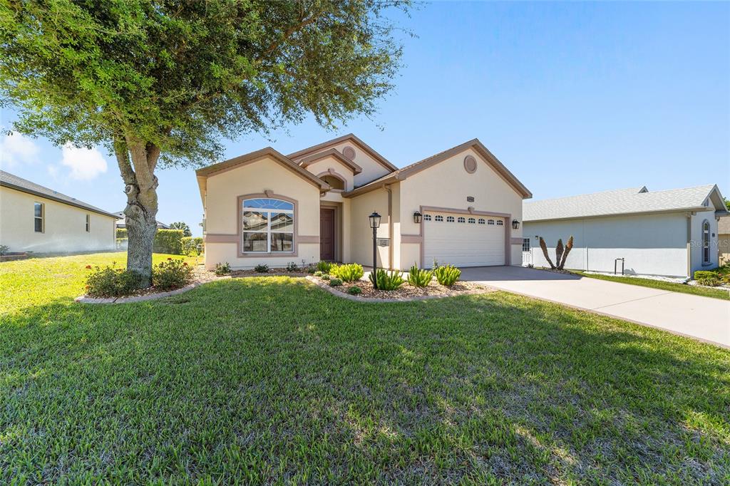 A single-story house with a beige stucco exterior, a two-car garage, and a front lawn — 10948 SE 167TH PLACE, SUMMERFIELD, FL