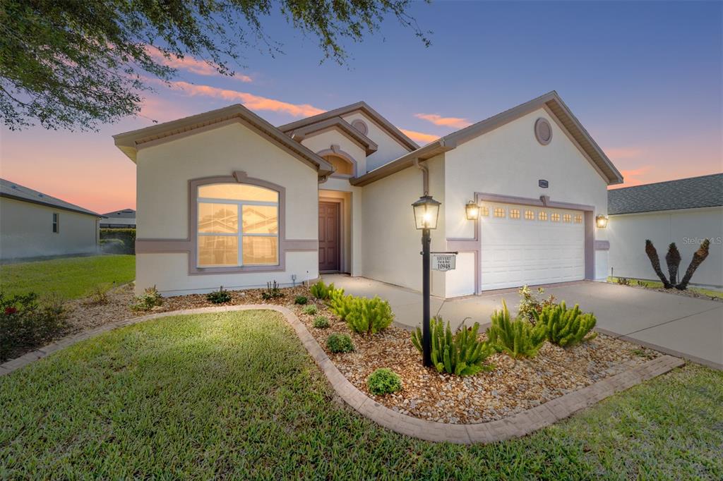 A single-story house with a beige stucco exterior, a two-car garage, and a landscaped yard — 10948 SE 167TH PLACE, SUMMERFIELD, FL