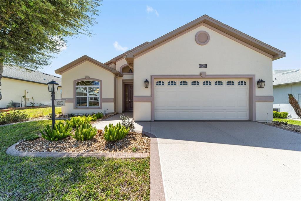 A single-story house with a beige stucco exterior, a two-car garage, and a landscaped yard — 10948 SE 167TH PLACE, SUMMERFIELD, FL