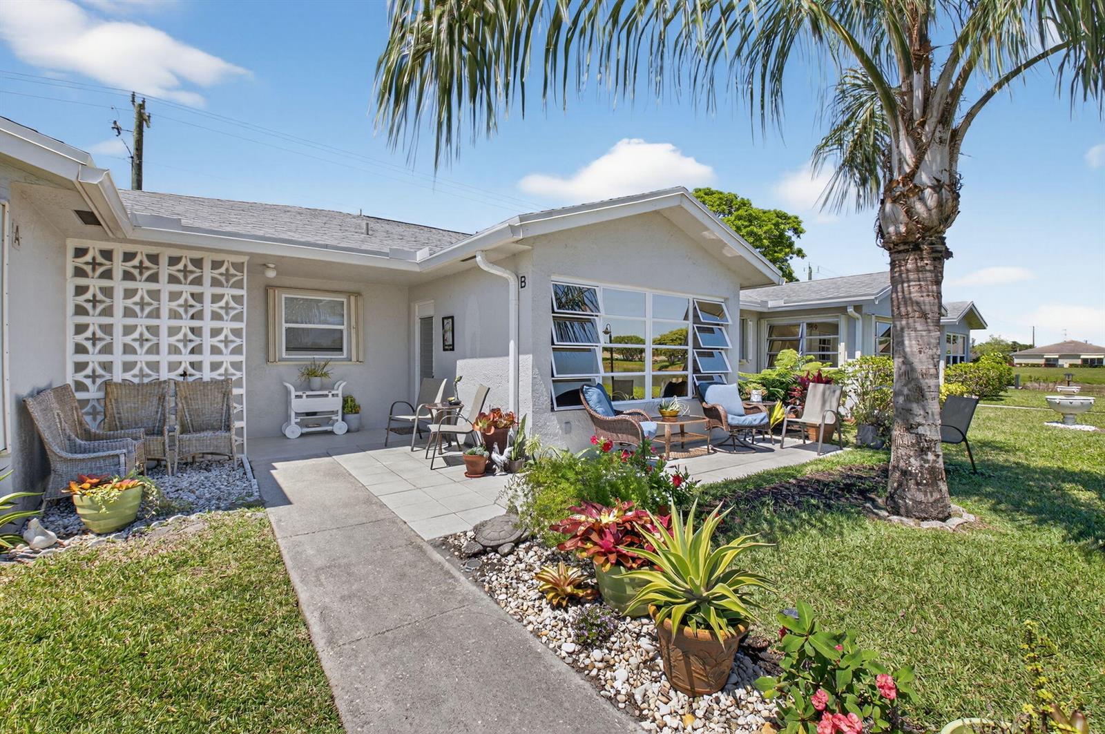 The exterior of a single-story residential building features a patio, landscaping, and a palm tree — 14519 Canalview Drive # B, Delray Beach FL 33484, DELRAY BEACH, FL