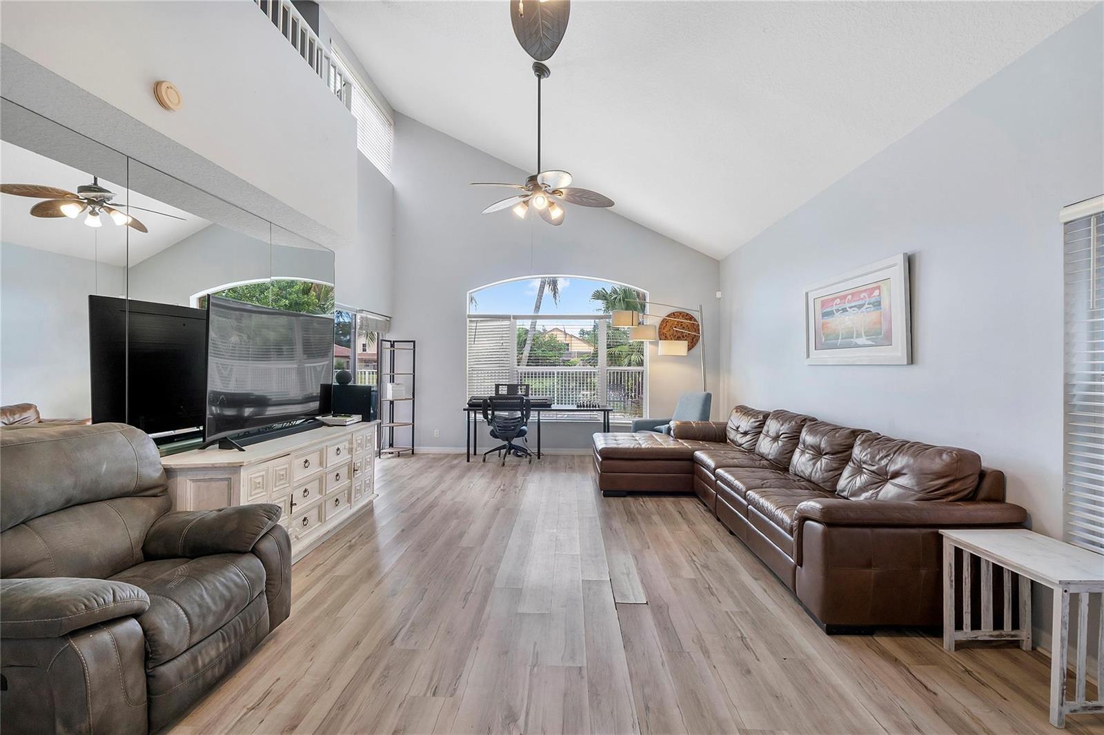 A living room with vaulted ceilings, wood-look flooring, a large sectional sofa, and a television — 4020 Dorado Drive, Riviera Beach FL 33418, RIVIERA BEACH, FL