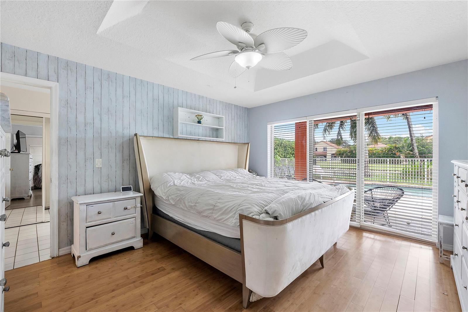 A bedroom features a white bed, light wood flooring, a ceiling fan, and sliding glass doors — 4020 Dorado Drive, Riviera Beach FL 33418, RIVIERA BEACH, FL