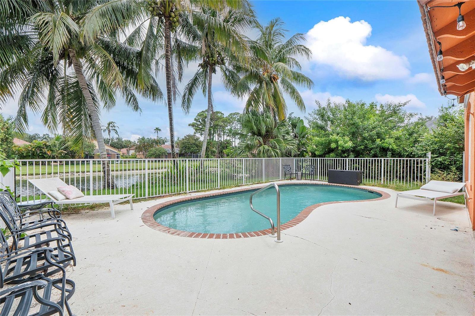 A kidney-shaped swimming pool sits on a concrete patio with lounge chairs and palm trees — 4020 Dorado Drive, Riviera Beach FL 33418, RIVIERA BEACH, FL