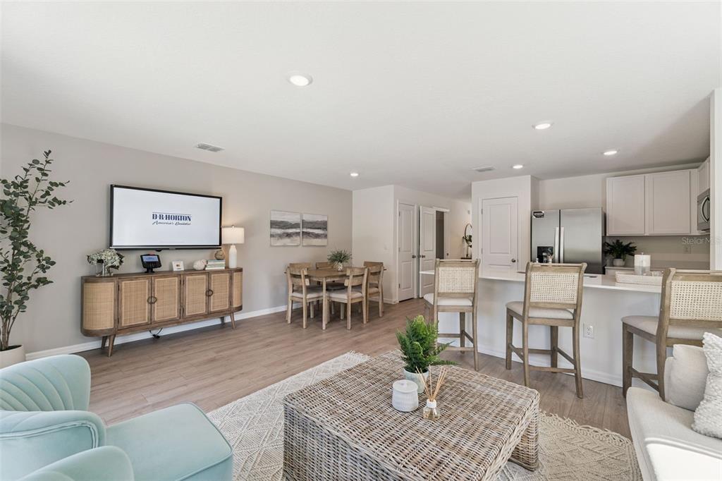 An open-concept living and dining area features light wood flooring, neutral walls, and a kitchen island — 1664 GREAT OSPREY WAY, NEW SMYRNA BEACH, FL