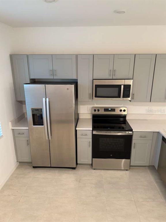 A kitchen features gray cabinets, stainless steel appliances, and light-colored tile flooring — 3184 SKYLINE LOOP, POINCIANA, FL