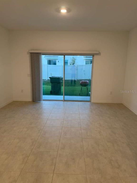 A room with light-colored tile flooring and a sliding glass door leading to a backyard — 3184 SKYLINE LOOP, POINCIANA, FL