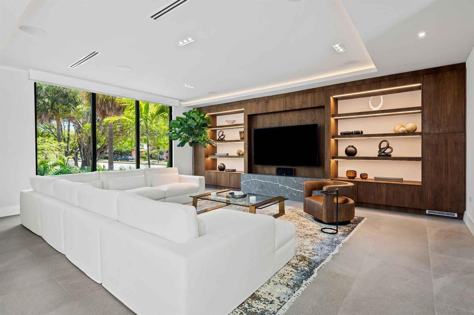 A modern living room features a large white sectional, wood-paneled media wall, and floor-to-ceiling windows — 5288 Alton Road # 3, Miami Beach FL 33140, MIAMI BEACH, FL