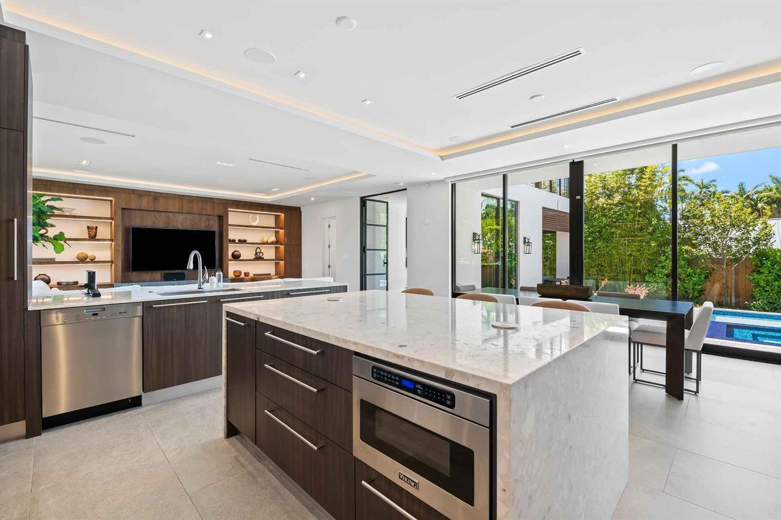 A modern kitchen features a marble-topped island, dark wood cabinetry, and large sliding glass doors — 5288 Alton Road # 3, Miami Beach FL 33140, MIAMI BEACH, FL