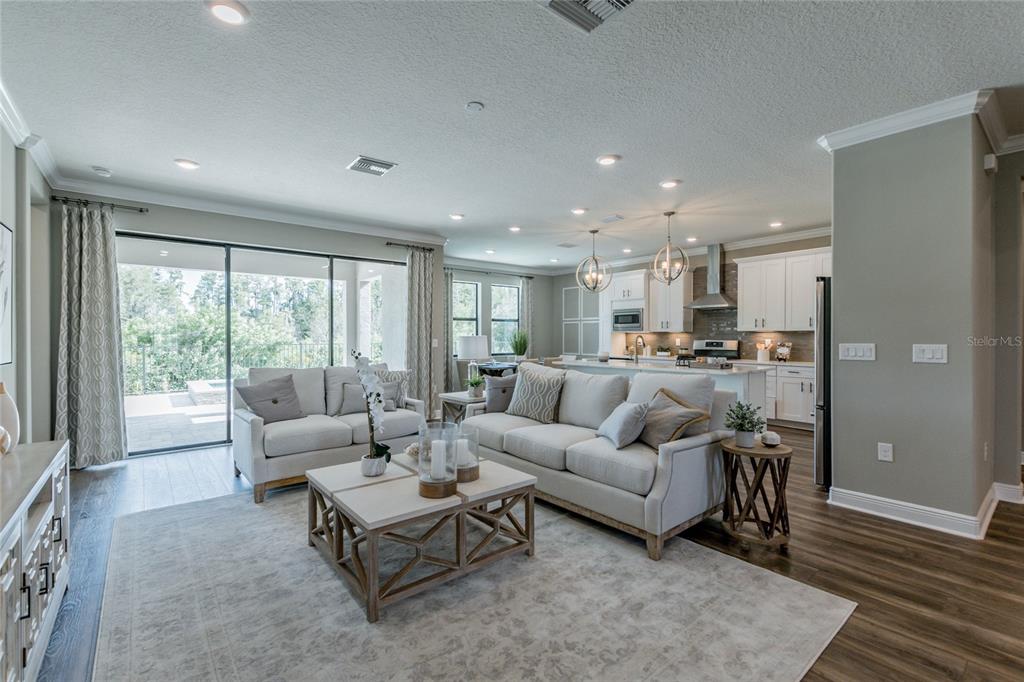 An open-concept living room and kitchen feature light-colored furniture, wood-look flooring, and sliding glass doors — 704 ESTATES BOULEVARD, TARPON SPRINGS, FL