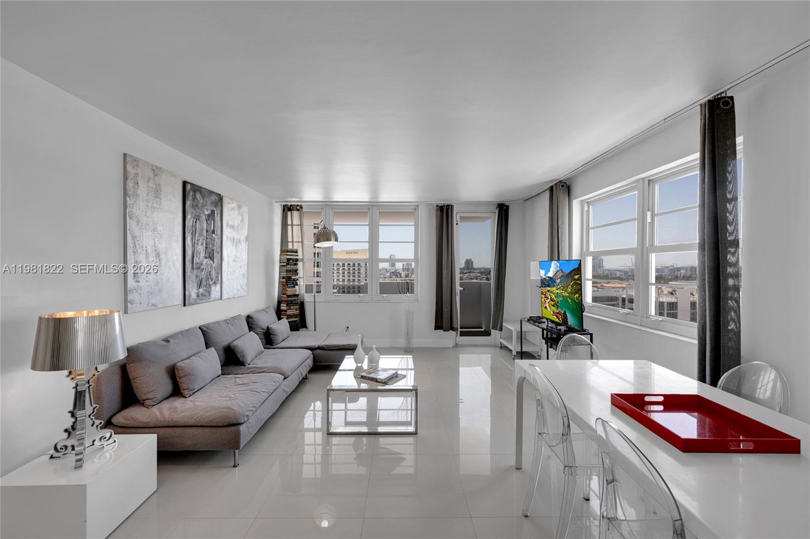A bright living and dining area features white tile floors, a gray sectional, and windows — 100 Lincoln Rd # 1511, Miami Beach FL 33139, MIAMI BEACH, FL