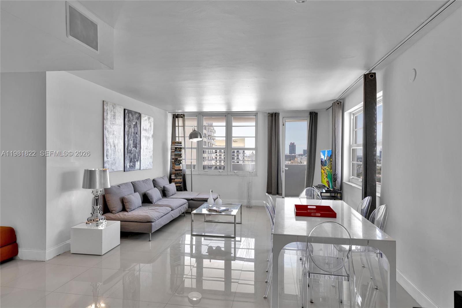 A bright living and dining area features white tile floors, a gray sofa, and windows — 100 Lincoln Rd # 1511, Miami Beach FL 33139, MIAMI BEACH, FL