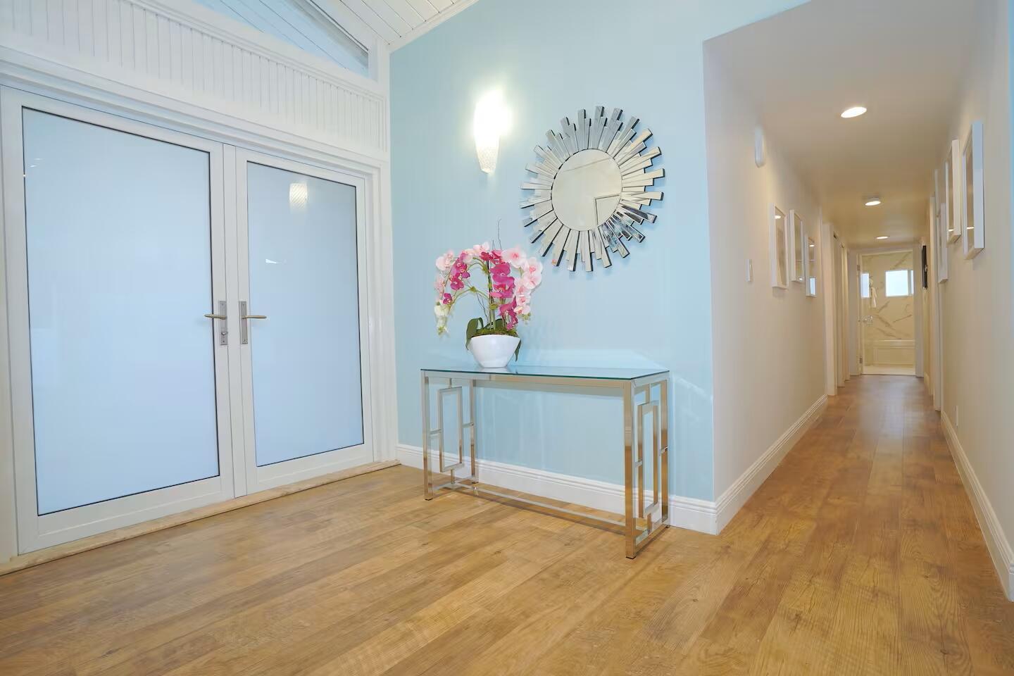 A light blue entryway features a glass console table, a sunburst mirror, and wood flooring — 1000 NE 8th Street, Pompano Beach FL 33060, POMPANO BEACH, FL