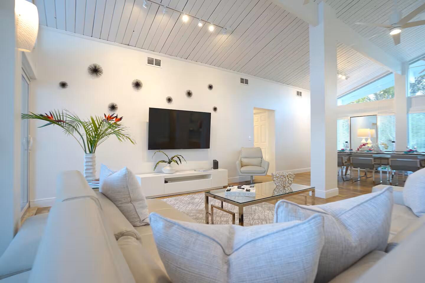 A bright living room features white walls, a vaulted ceiling, and a modern television console — 1000 NE 8th Street, Pompano Beach FL 33060, POMPANO BEACH, FL