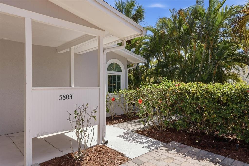 A paved walkway leads to the covered entryway of a house with light-colored siding — 5803 DE PALMAS AVENUE, HOLMES BEACH, FL
