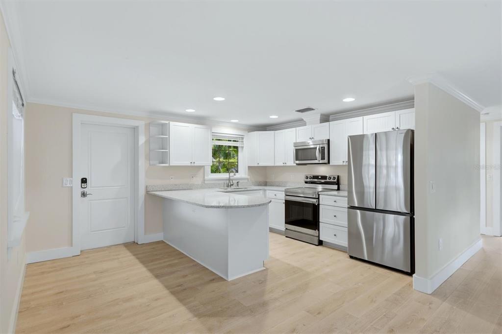 A kitchen with white cabinets, stainless steel appliances, granite countertops, and light wood-look flooring — 5803 DE PALMAS AVENUE, HOLMES BEACH, FL