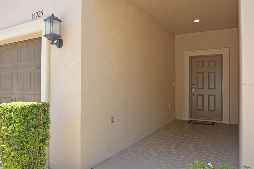 A covered entryway features a brown front door, a garage door, and a brick-patterned floor — 11925 GREENGATE DRIVE, HUDSON, FL