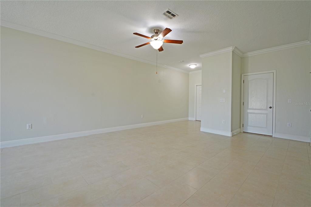 A spacious, empty room features light-colored tile flooring, a ceiling fan, and white walls — 11925 GREENGATE DRIVE, HUDSON, FL