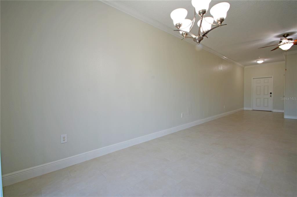 A long, empty room features light-colored tile flooring, a chandelier, and a white front door — 11925 GREENGATE DRIVE, HUDSON, FL