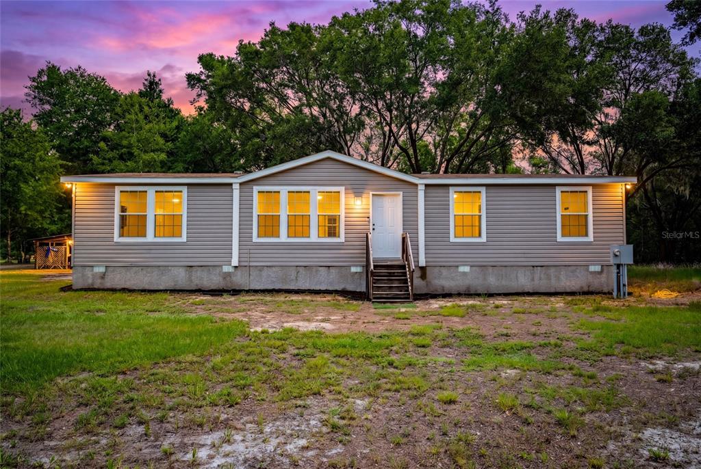 A single-story manufactured home with gray siding sits on a lot at sunset — 14002 BAY LAKE ROAD, GROVELAND, FL
