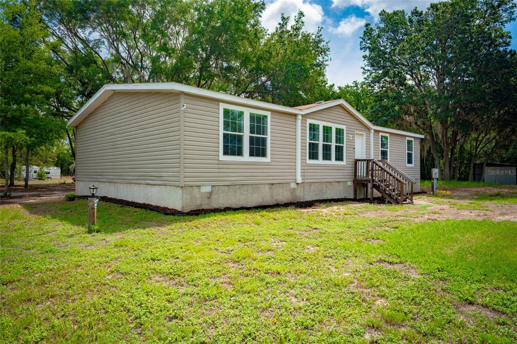 A tan, single-story manufactured home sits on a grassy lot surrounded by trees — 14002 BAY LAKE ROAD, GROVELAND, FL