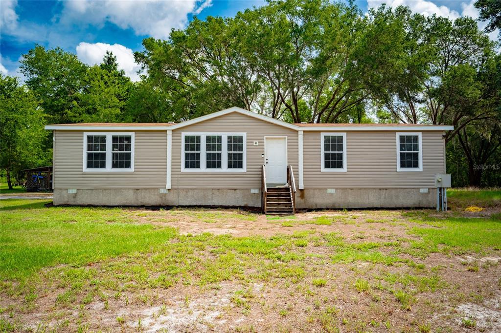A single-story manufactured home with tan siding and a front entrance with wooden steps — 14002 BAY LAKE ROAD, GROVELAND, FL