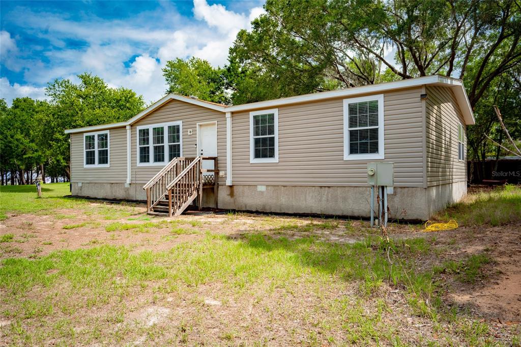 A tan, single-story manufactured home with vinyl siding stands on a grassy lot — 14002 BAY LAKE ROAD, GROVELAND, FL