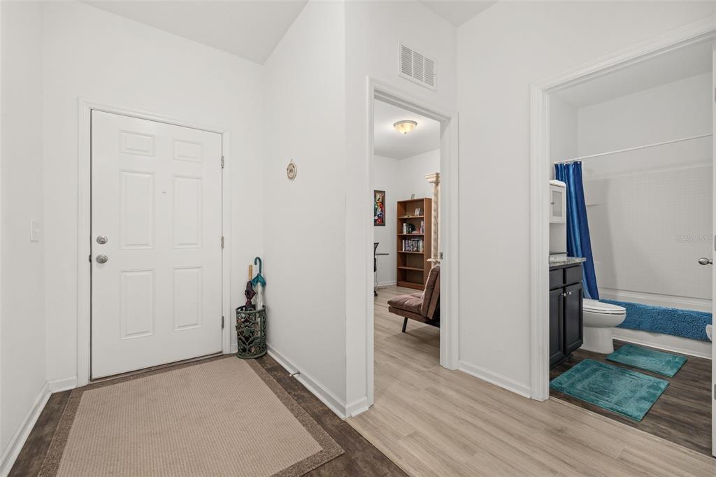 An entryway with a white front door, light wood flooring, and an adjacent bathroom — 15409 IVORY GULL LANE, MASCOTTE, FL