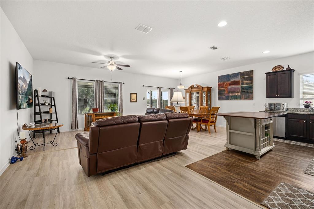 An open-concept living and dining area features wood-look flooring, a brown leather sofa, and kitchen — 15409 IVORY GULL LANE, MASCOTTE, FL
