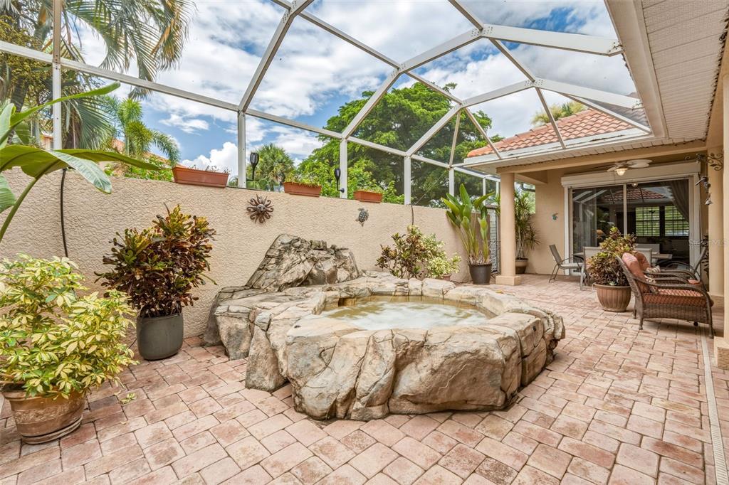 A screened-in patio features a rock-style hot tub, potted plants, and brick paver flooring — 13921 BENTLY CIRCLE, FORT MYERS, FL