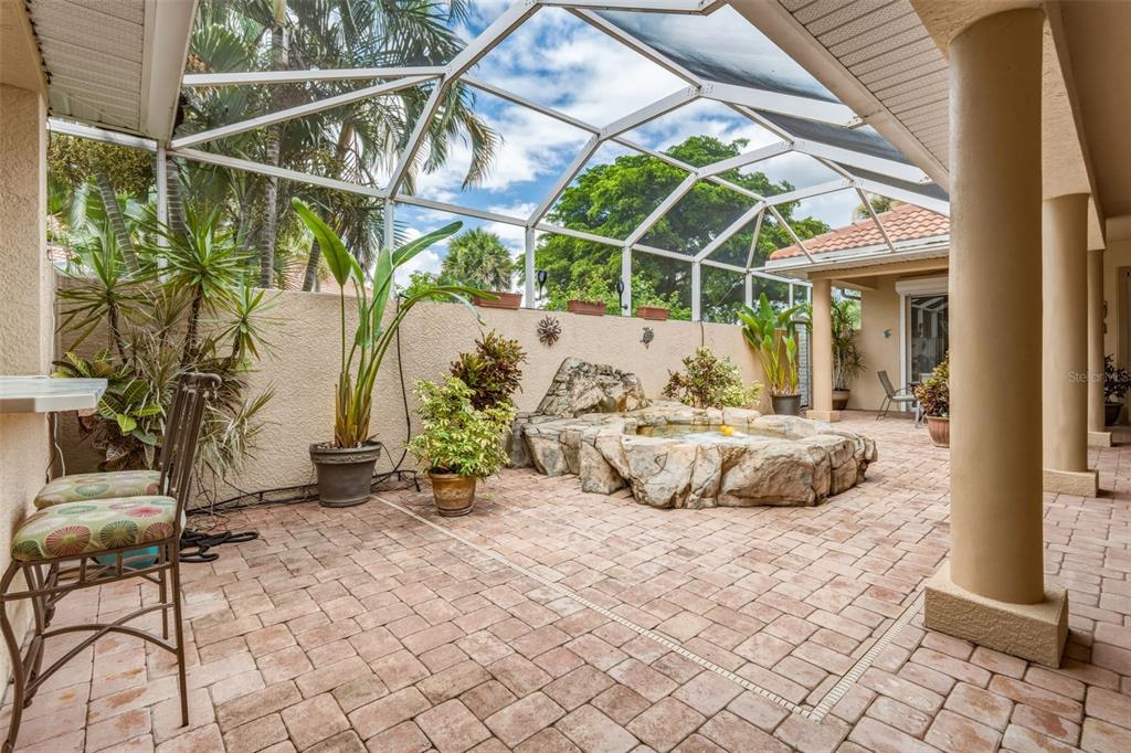 A screened-in patio features a stone-encased hot tub, brick pavers, and potted plants — 13921 BENTLY CIRCLE, FORT MYERS, FL