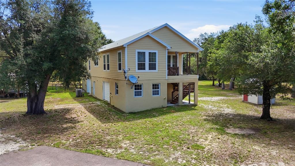 A two-story yellow house with a raised foundation and a side-entry garage sits outdoors — 11604 SE SHELFER AVENUE, ARCADIA, FL