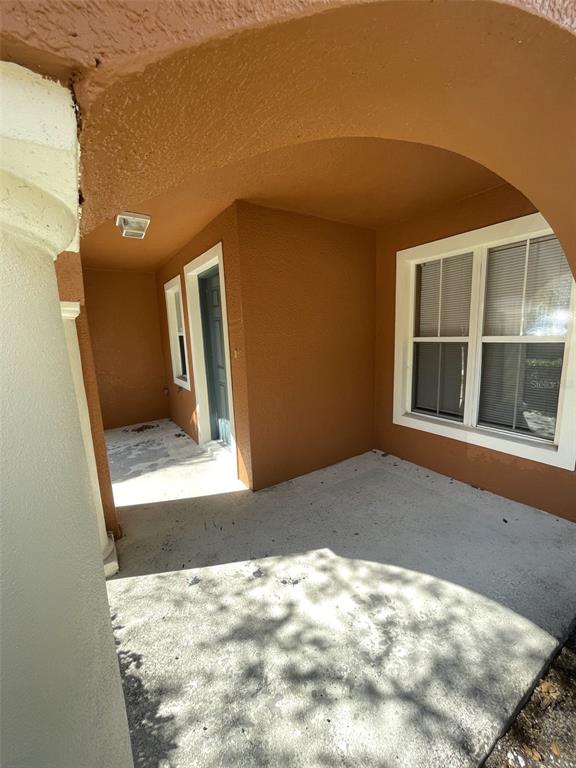 A covered concrete porch features a front door and a window with white trim — 10934 JOHANNA AVENUE, RIVERVIEW, FL