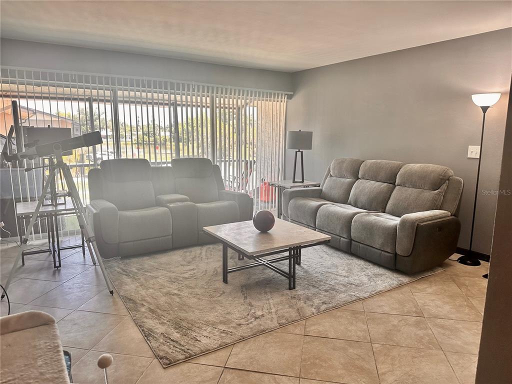 A living room features two gray sofas, a square coffee table, and a telescope — 2938 CLARK ROAD UNIT 203, SARASOTA, FL
