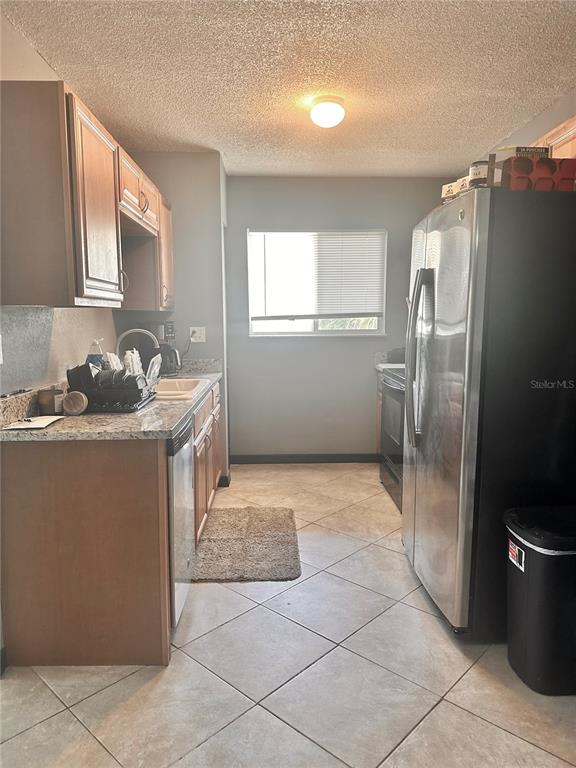 A galley kitchen features wood cabinets, granite countertops, tile flooring, and stainless steel appliances — 2938 CLARK ROAD UNIT 203, SARASOTA, FL