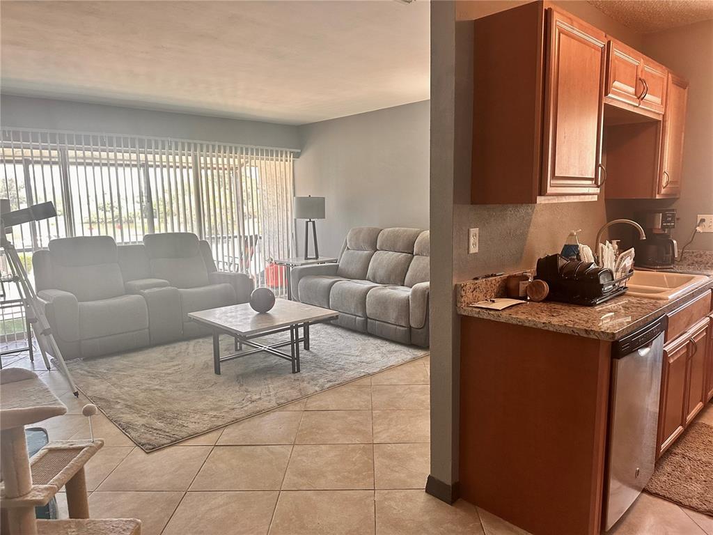 A living room with gray sofas and a kitchen with wood cabinets and granite countertops — 2938 CLARK ROAD UNIT 203, SARASOTA, FL
