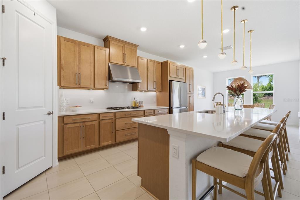A modern kitchen features light wood cabinets, white countertops, a large island, and pendant lighting — 16508 STAR GRASS CIRCLE, BRADENTON, FL
