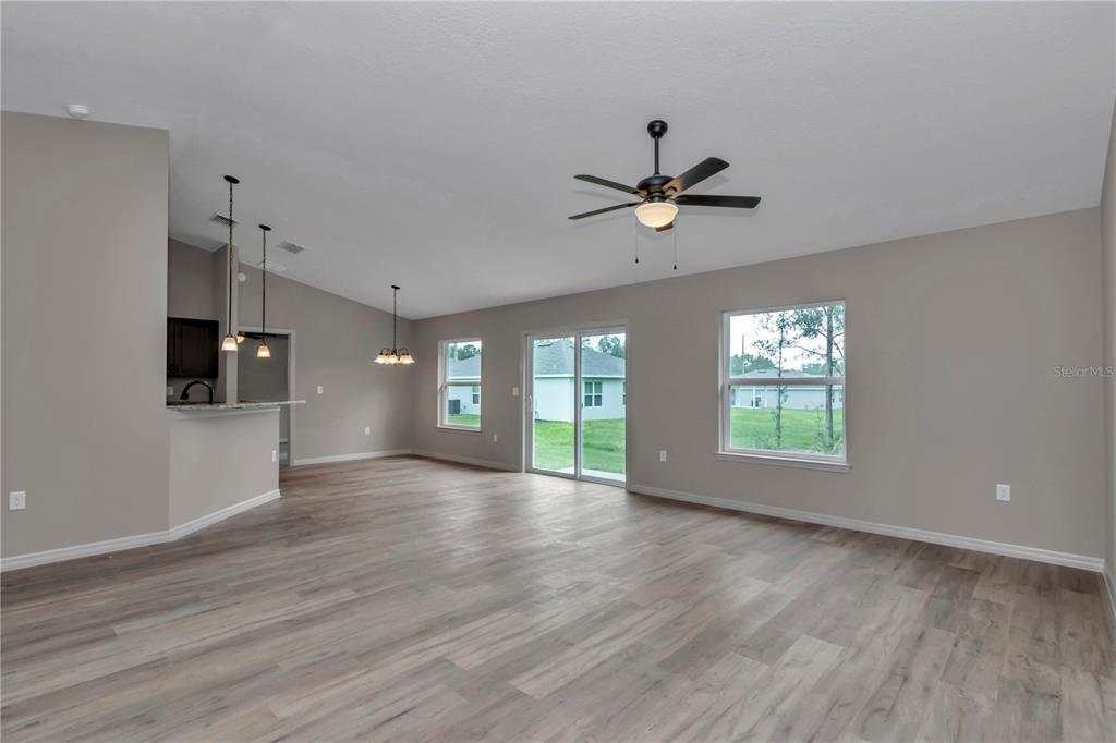 An open-concept living area features light wood-look flooring, a ceiling fan, and sliding glass doors — 14317 SW 78TH TERRACE, OCALA, FL
