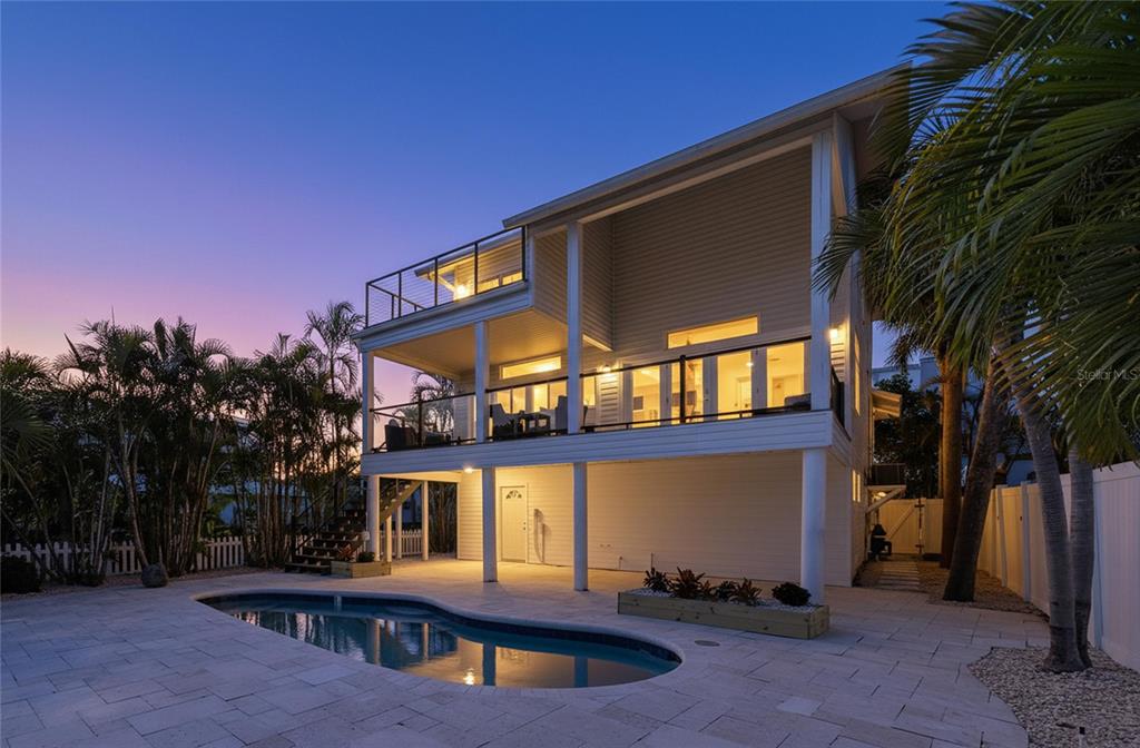 A two-story elevated house with a pool, balconies, and palm trees at twilight — 8485 BLIND PASS DRIVE, TREASURE ISLAND, FL